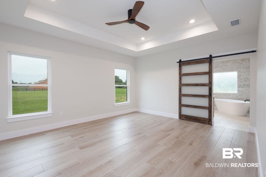 13066 Gopher Court Elberta, AL 36530 - Photo 11 of 38 Spacious Primary bedroom featuring wood-finish flooring, a tray ceiling with recessed lighting, and a modern ceiling fan. The sliding door leads you to your glamorous ensuite.