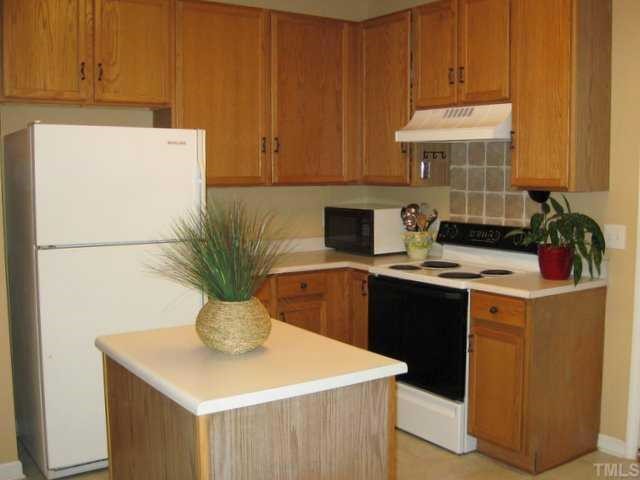 1316 Red Twig Road Apex, NC 27502 - Photo 4 of 12 The warm golden hue of wood cabinetry and a decorative tile backsplash enhance the well arranged kitchen of this home. A door from the kitchen leads to a very useful, separate workshop-mudroom area with lots of built-in shelving and storage space.