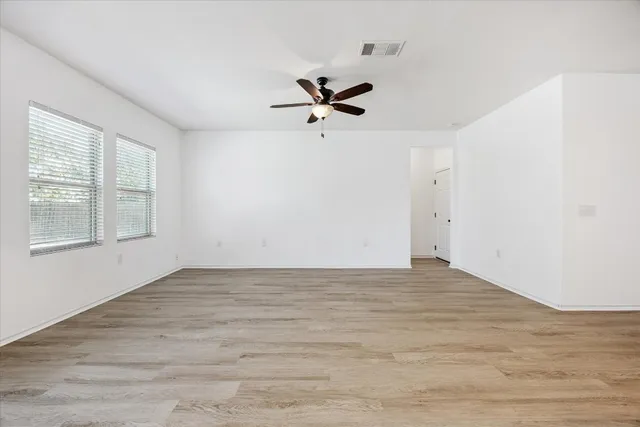 an empty room with wooden floor ceiling fan and windows