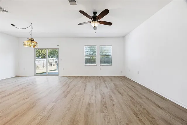 an empty room with wooden floor chandelier fan and windows
