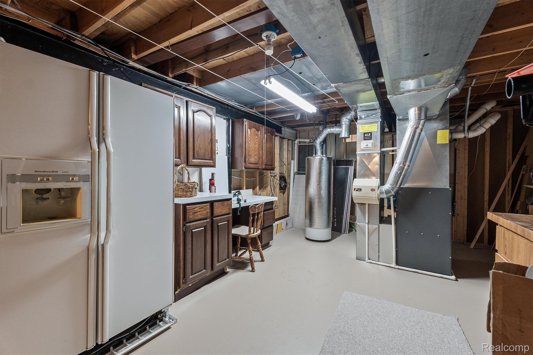 1662 Sumac Drive Rochester, MI 48309 - Photo 29 of 38 Finished lower level featuring exposed ceiling joists, ample cabinetry with countertop space, two large white refrigerators, a water heater, and a furnace with exposed ductwork