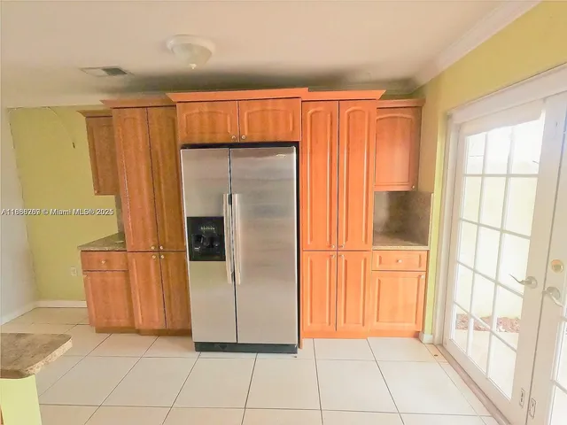a view of a refrigerator in kitchen and an empty room with wooden floor