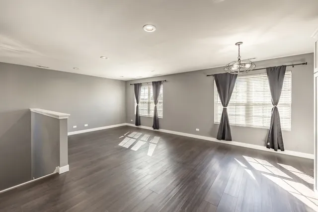 an empty room with wooden floor chandelier and windows