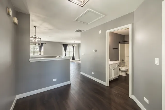 a view of a kitchen from the hallway with wooden floor and a bathroom