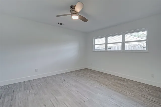 an empty room with wooden floor fan and windows