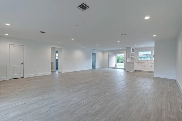 a view of an empty room and a kitchen with wooden floor