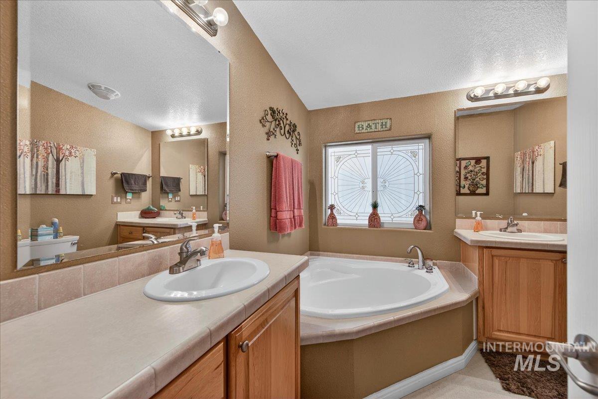 421 South Curtis Road, Unit 118 Boise, ID 83705 - Photo 32 of 49 Bathroom featuring two vanities, a bath, a textured wall, and a textured ceiling