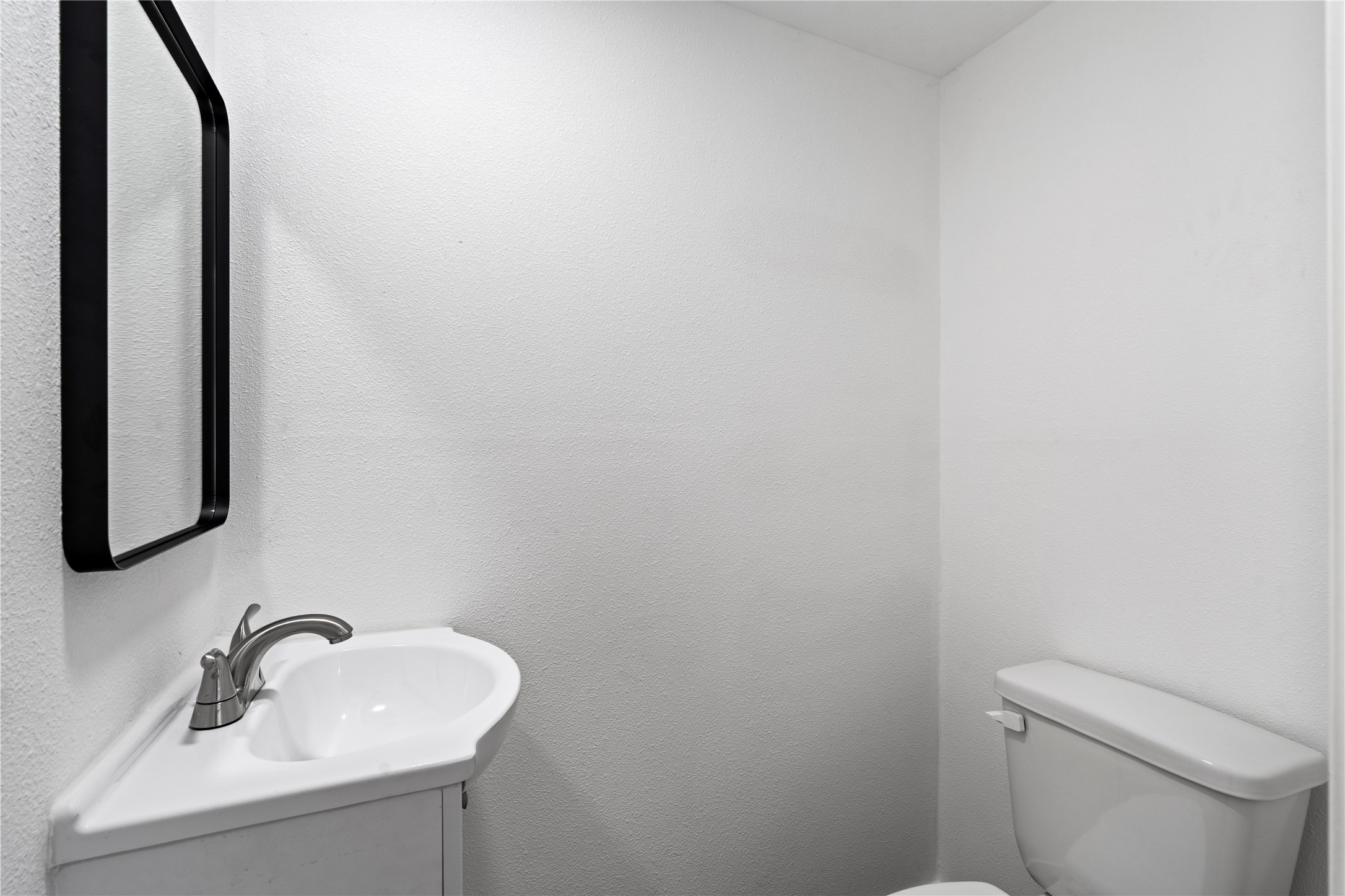 5023 Redstart Street Houston, TX 77035 - Photo 22 of 34 A minimalist half-bath offers clean lines with a modern corner pedestal sink and a high-contrast black-framed mirror, perfect for guests.