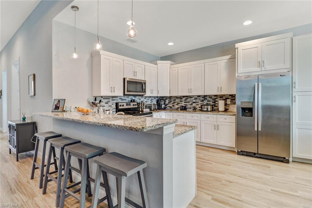 8476 Grove Road Fort Myers, FL 33967 - Photo 4 of 25 a kitchen with kitchen island granite countertop a refrigerator a stove a sink and white cabinets with wooden floor