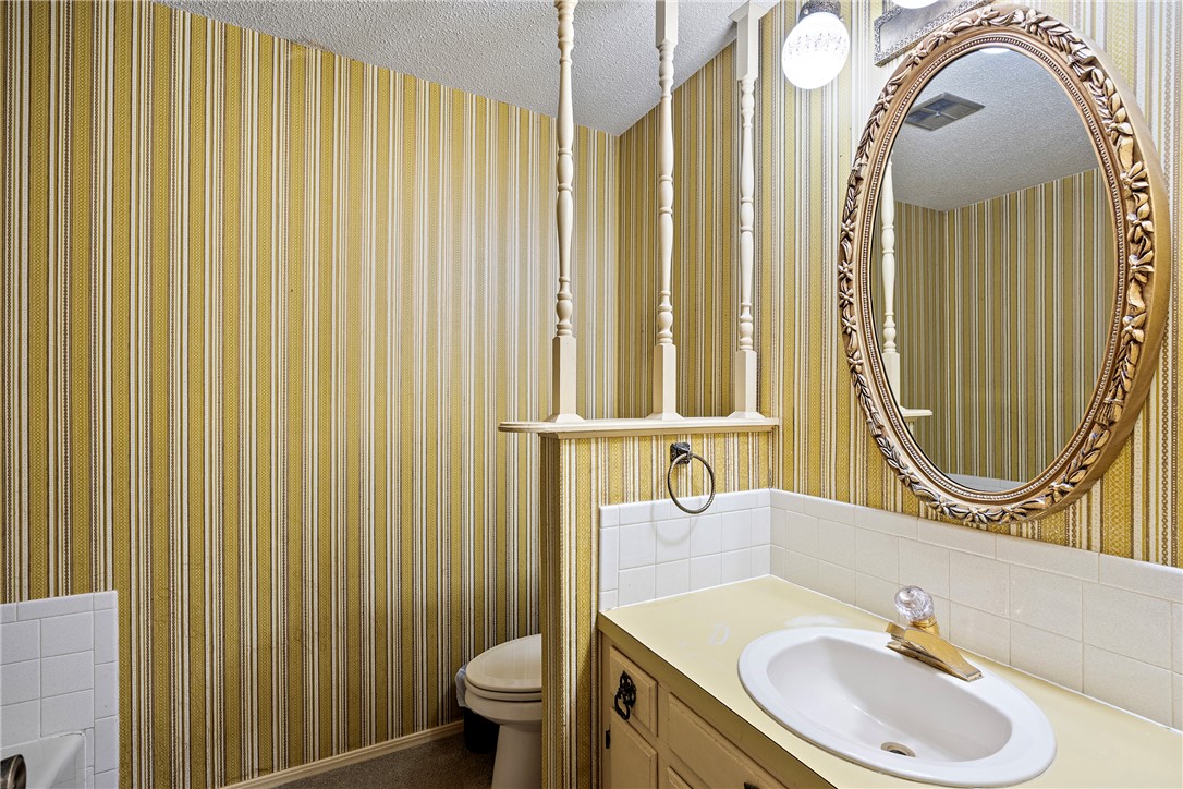 411 Marina Road Russellville, AR 72802 - Photo 17 of 49 Bathroom featuring a single vanity with an oval sink, a wall-mounted oval mirror with an ornate frame, a ceramic tile backsplash, and striped wallpaper