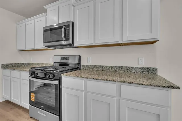 a kitchen with stainless steel appliances granite countertop white cabinets and a stove top oven
