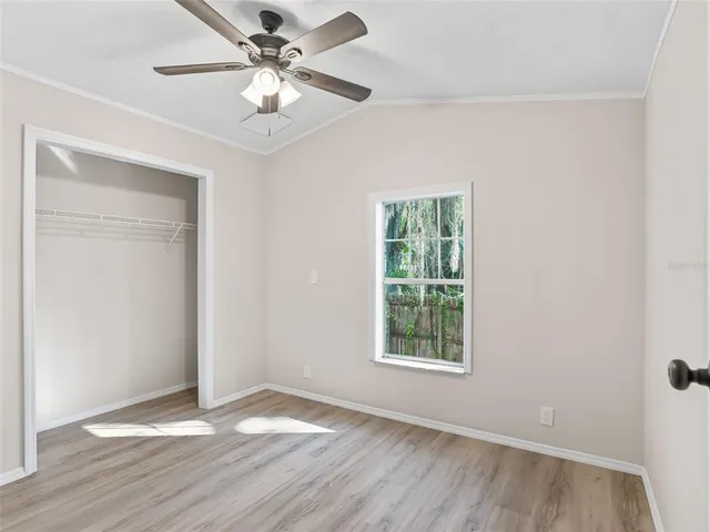 an empty room with wooden floor chandelier fan and windows