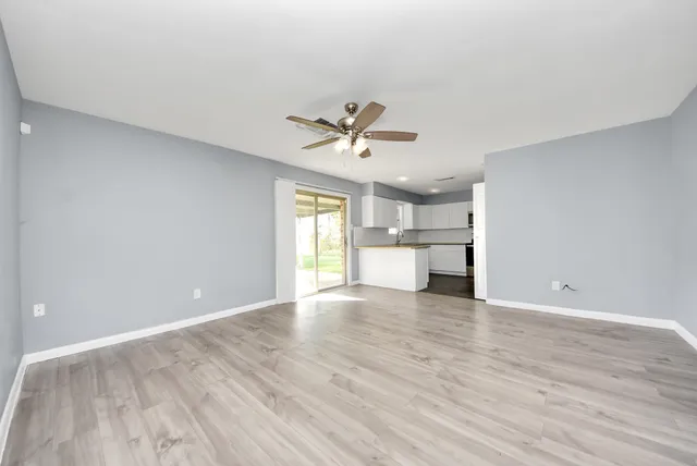 a view of an empty room with a window and a kitchen with wooden floor