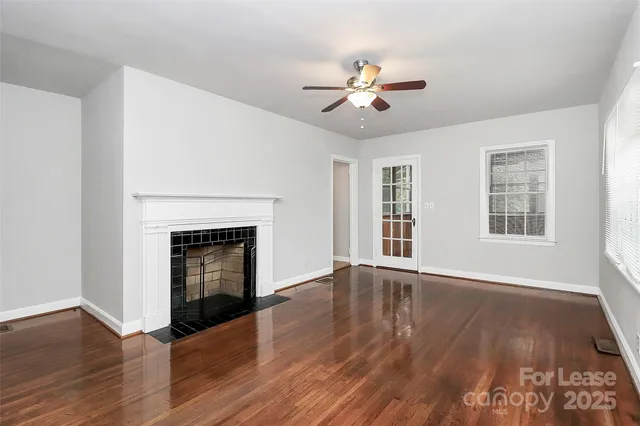 a view of an empty room with wooden floor fireplace and a window