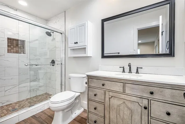 a bathroom with a toilet a sink a glass door a shower a mirror and vanity