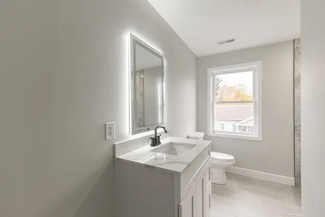 a bathroom with a granite countertop sink a toilet and a window