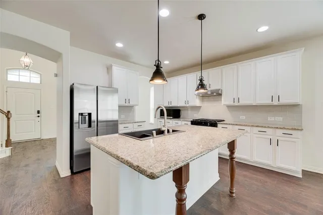 a kitchen with stainless steel appliances kitchen island granite countertop a sink a stove a refrigerator and white cabinets