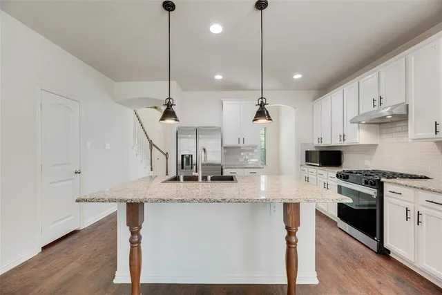 a kitchen with stainless steel appliances granite countertop a sink a stove a refrigerator and island with wooden floor