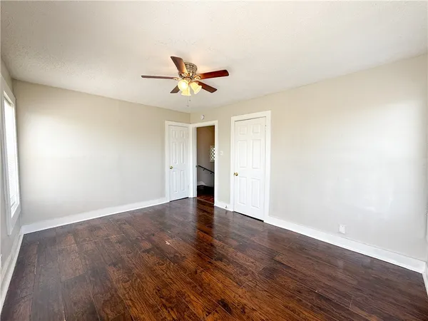 a view of an empty room with wooden floor and a ceiling fan