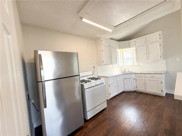 a kitchen with stainless steel appliances a refrigerator a sink a stove and white cabinets with wooden floor