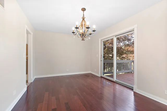 an empty room with wooden floor chandelier and windows