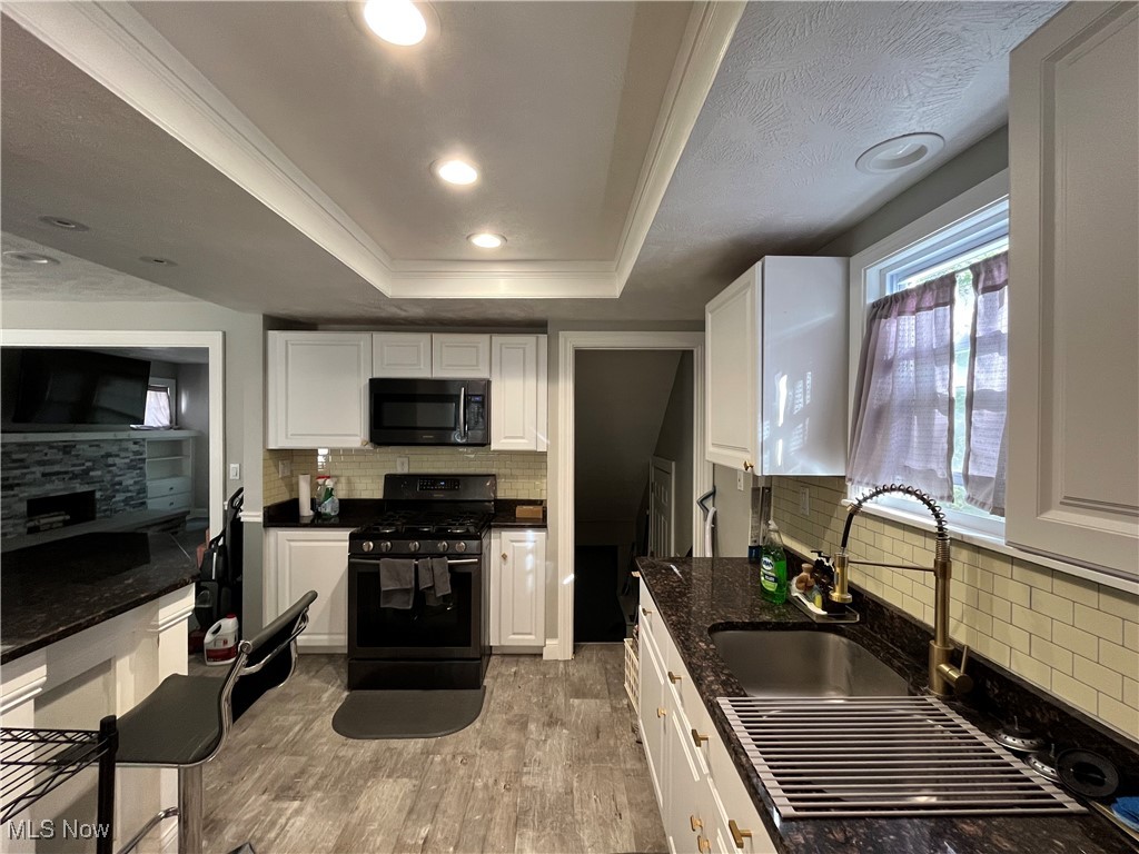 1048 Pembrook Road Cleveland, OH 44121 - Photo 11 of 26 Kitchen with backsplash, white cabinetry, black appliances, a tray ceiling, and light hardwood / wood-style floors