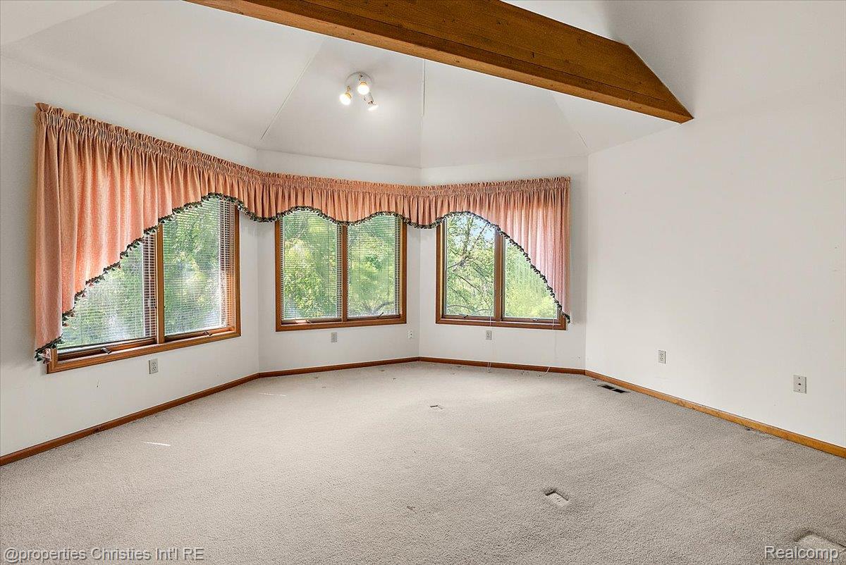 6175 Tripp Road Holly, MI 48442 - Photo 14 of 63 Spacious room featuring a vaulted ceiling with exposed wood beams, a bay window with wood trim, wall-to-wall carpeting, and track lighting