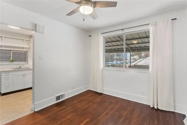 an empty room with wooden floor chandelier fan and windows