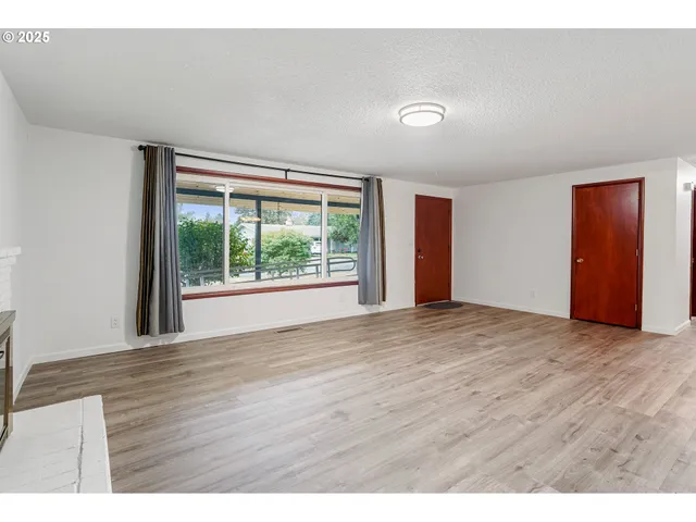 a view of an empty room with wooden floor and window