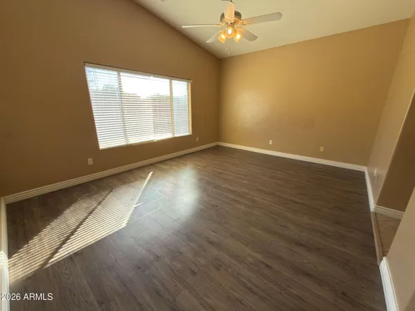 an empty room with wooden floor chandelier fan and windows