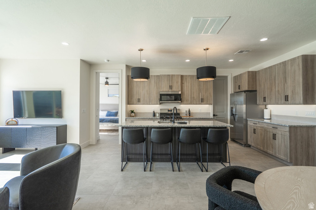 2972 West 570 North Hurricane, UT 84737 - Photo 24 of 104 Kitchen featuring light stone countertops, a breakfast bar area, an island with sink, hanging light fixtures, and stainless steel appliances