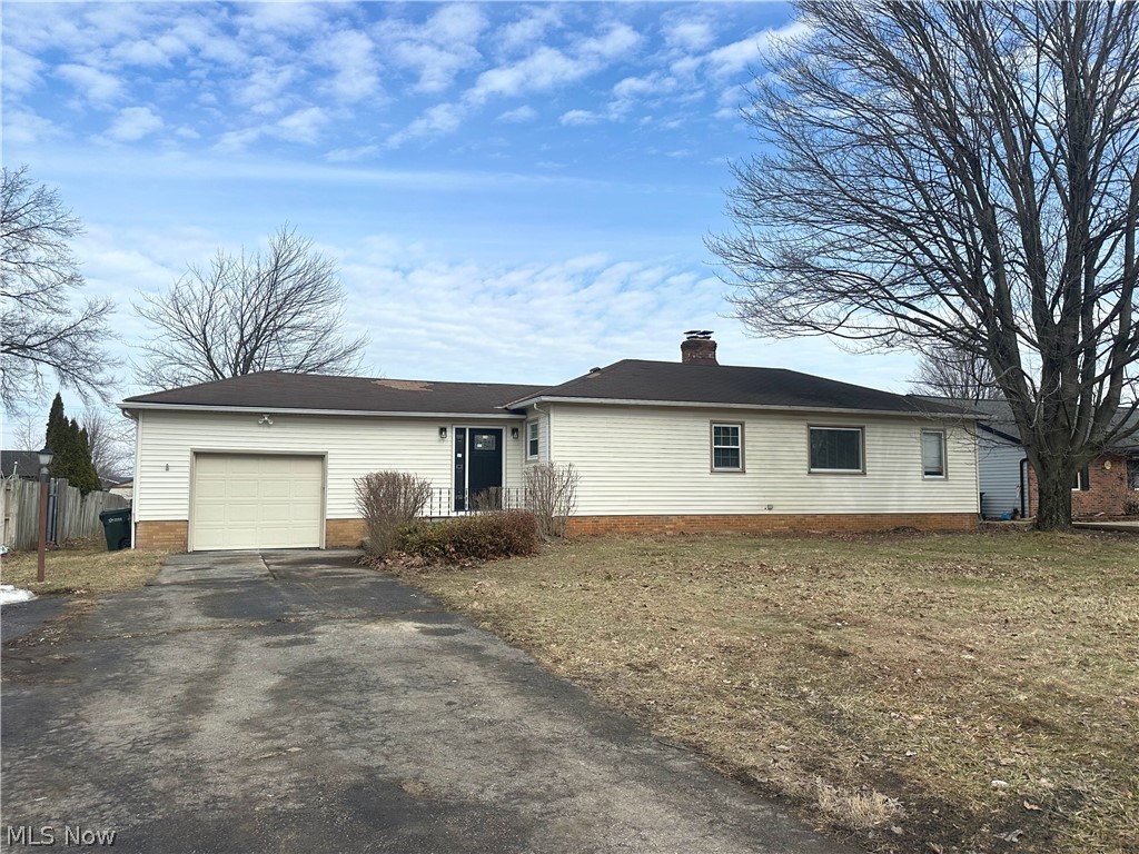 Single story home featuring a chimney, a garage, asphalt driveway, and brick siding