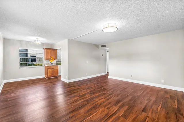 an empty room with wooden floor and kitchen view