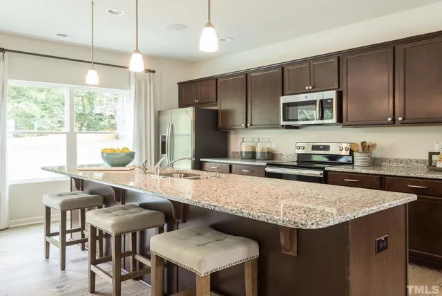 a kitchen with stainless steel appliances granite countertop a stove top oven a sink a dining table and chairs with wooden floor