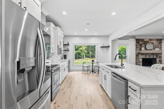 a large kitchen with stainless steel appliances a stove a sink dishwasher a refrigerator white cabinets and wooden floor