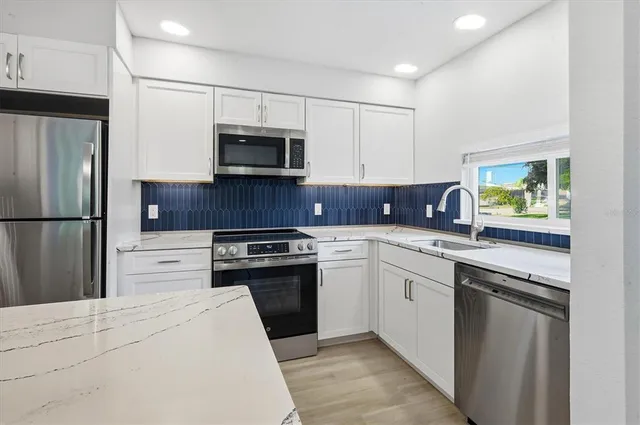 a kitchen with stainless steel appliances granite countertop a refrigerator stove a sink and a oven with wooden floor