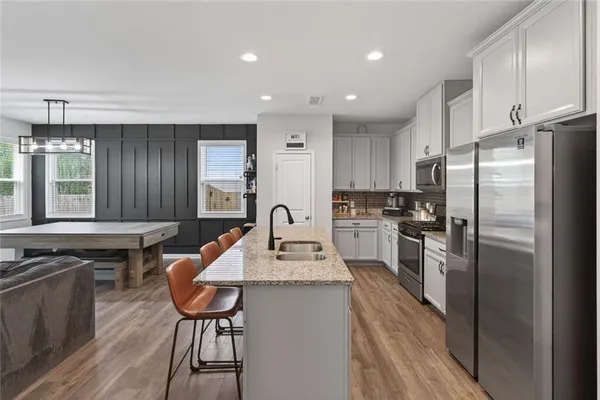 a kitchen with stainless steel appliances a refrigerator a stove a sink a dining table and chairs with wooden floor