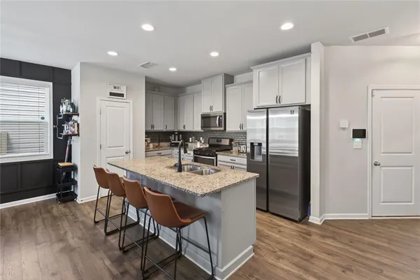 a kitchen with stainless steel appliances granite countertop a dining table chairs refrigerator and sink