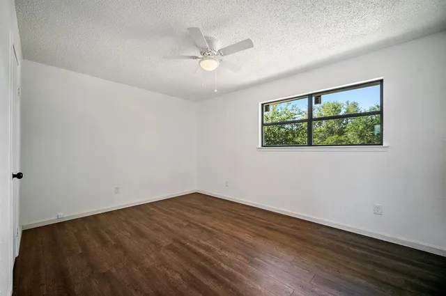 an empty room with wooden floor ceiling fan and windows