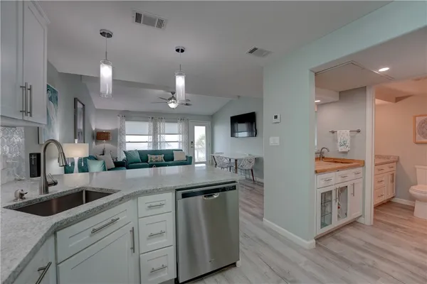 a kitchen with stainless steel appliances white cabinets a sink dishwasher and a stove with wooden floor