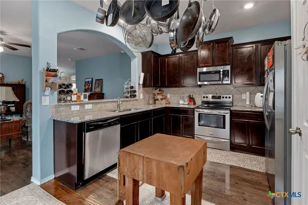 a kitchen with stainless steel appliances granite countertop a sink dishwasher a stove refrigerator and microwave with wooden floor