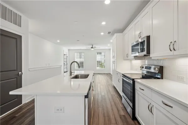 a kitchen with stainless steel appliances a stove top oven a sink a refrigerator white cabinets and wooden floor