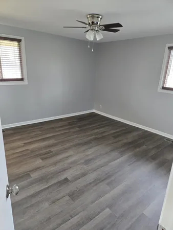 an empty room with wooden floor fan and windows