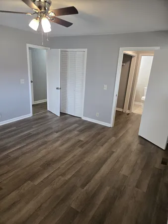 a view of an empty room with wooden floor and a ceiling fan