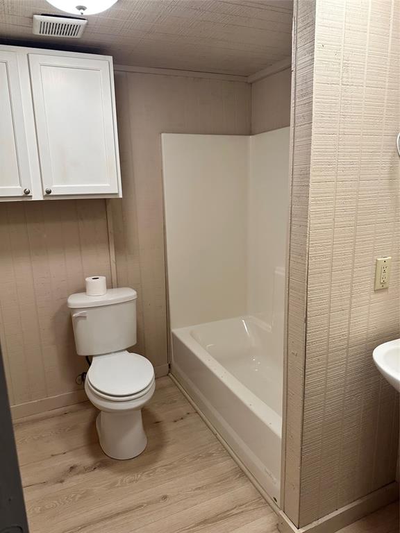 2590 Rock Ridge Road Lucas, TX 75002 - Photo 22 of 25 Bathroom featuring a white toilet, integrated bathtub and shower unit, wood-finish flooring, and white upper cabinetry
