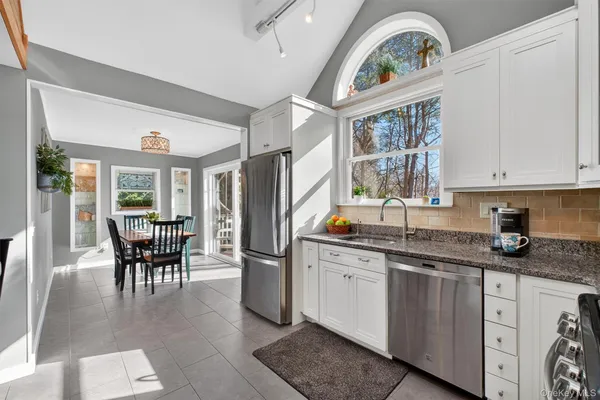 a kitchen with stainless steel appliances granite countertop a stove a sink dishwasher and white cabinets with wooden floor