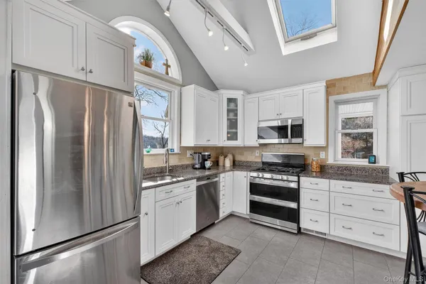 a kitchen with stainless steel appliances granite countertop a refrigerator a stove a sink dishwasher and white cabinets with wooden floor