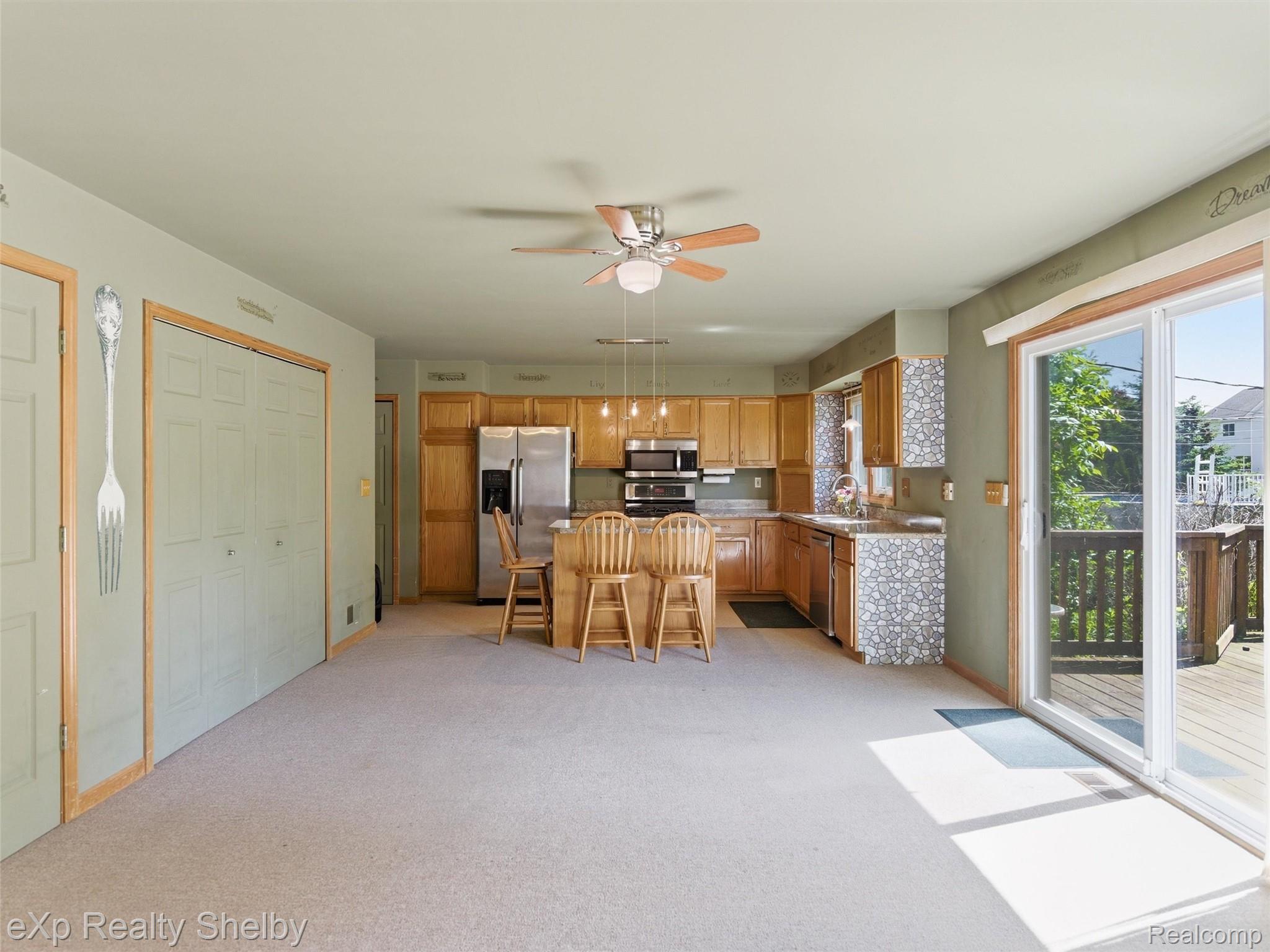 4154 Union Street Dryden, MI 48428 - Photo 14 of 41 Open-concept kitchen and living area featuring wood cabinetry, an island with pendant lighting, stainless steel appliances, and a sliding glass door to an outdoor deck