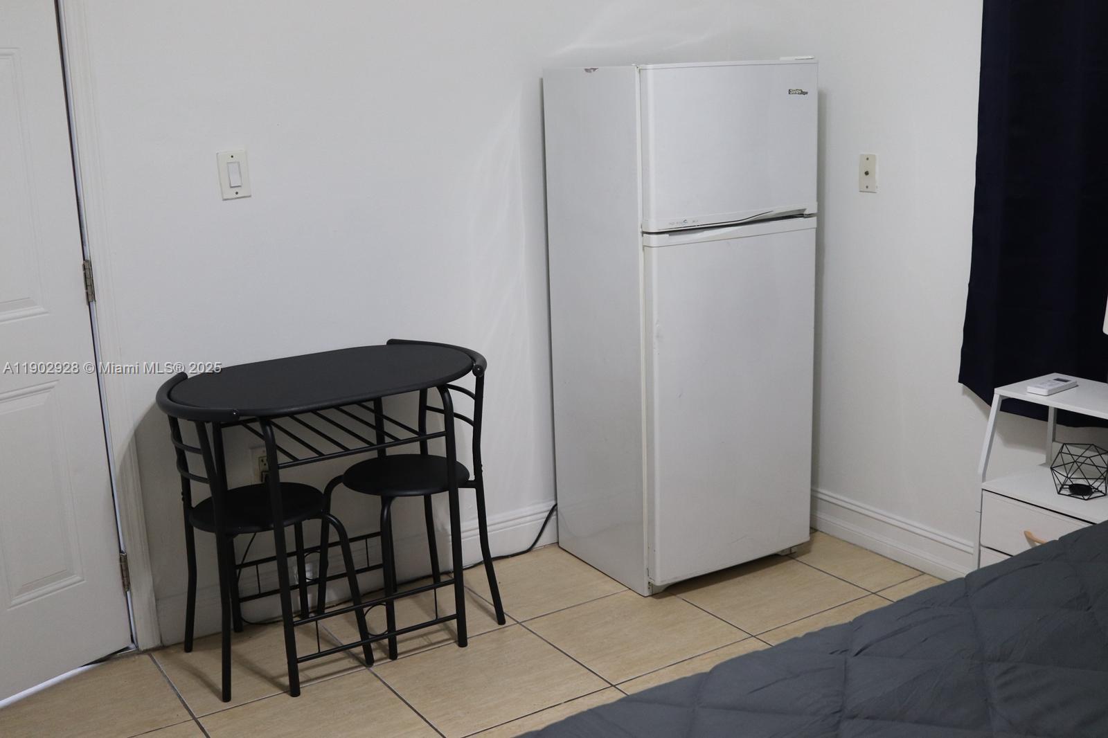 20022 Northwest 58th Court, Unit 1 Hialeah, FL 33015 - Photo 6 of 12 a view of a refrigerator in kitchen and an empty room with wooden floor