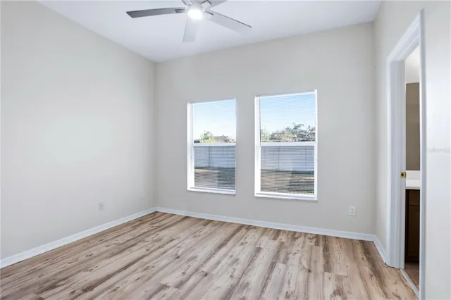 an empty room with wooden floor and way to kitchen